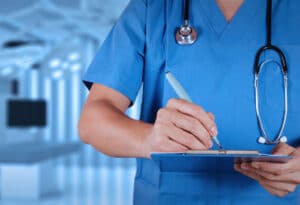 immagine ravvicinata di un medico con camice blu che scrive su una cartellina 