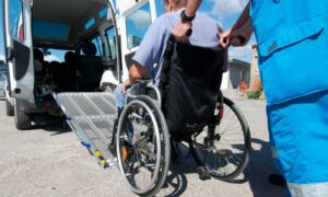 un operatore aiuta una persona anziana su carrozzina a salire su un mezzo sanitario con rampa